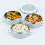 Trois bols inox de la lunch box ronde remplis de légumes, de poulet et de riz, avec leur couvercle