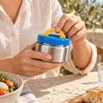 Femme qui ouvre un mini pot isotherme inox à couvercle bleu, à une table en terrasse