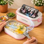 Lunch box rose ouverte avec riz et œuf, cuillère pliante et téléphone posé sur le couvercle